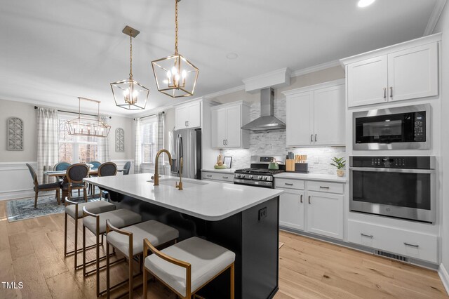 kitchen featuring a breakfast bar area, stainless steel appliances, ornamental molding, wall chimney exhaust hood, and an island with sink