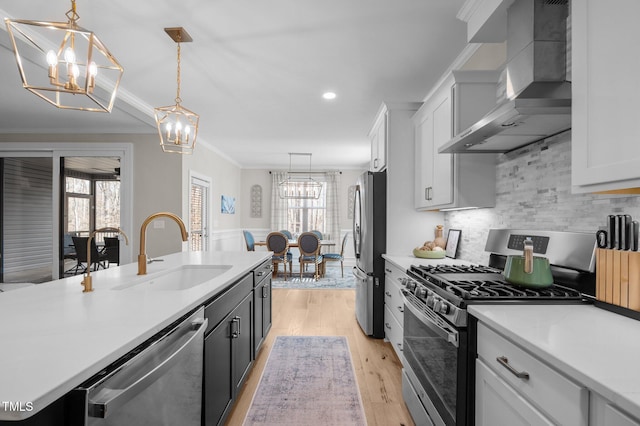 kitchen featuring appliances with stainless steel finishes, a sink, wall chimney exhaust hood, and an inviting chandelier