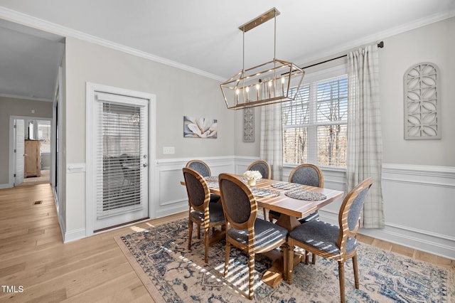 dining space with a wainscoted wall, light wood-style floors, an inviting chandelier, and crown molding