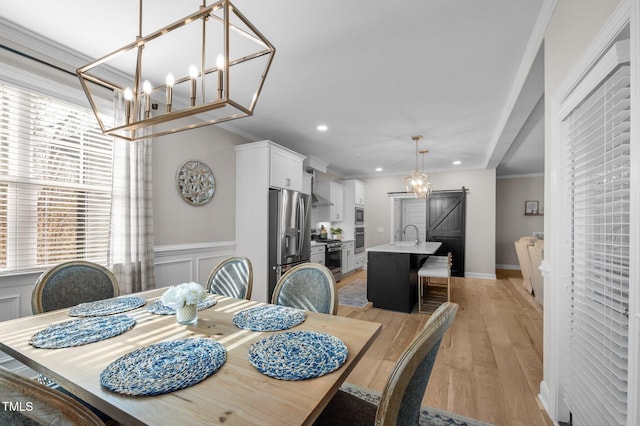 dining space with a wainscoted wall, a decorative wall, a barn door, ornamental molding, and light wood-type flooring