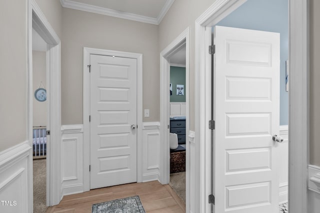 interior space featuring light wood-style floors, a decorative wall, wainscoting, and crown molding