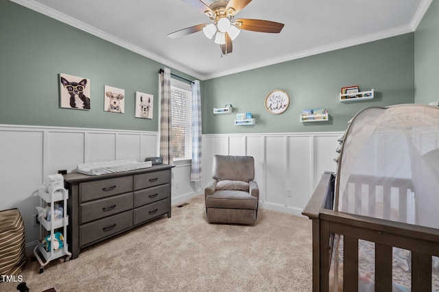 carpeted bedroom with a wainscoted wall, ornamental molding, and a ceiling fan