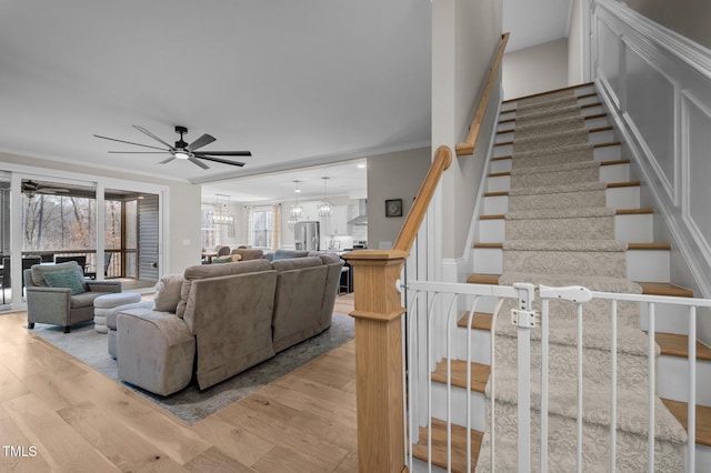 living room with stairs, ceiling fan with notable chandelier, light wood-type flooring, and crown molding