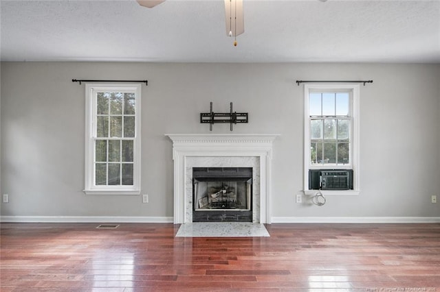 unfurnished living room featuring cooling unit, a healthy amount of sunlight, a high end fireplace, and hardwood / wood-style floors