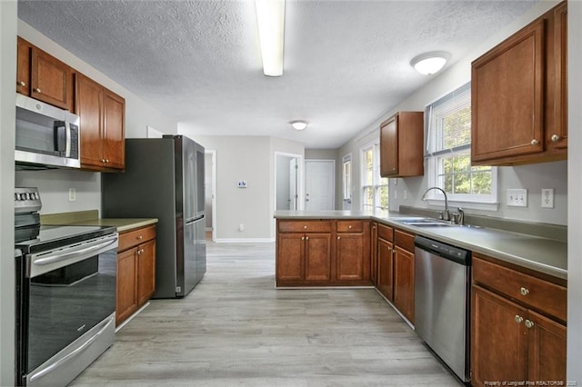 kitchen with appliances with stainless steel finishes, sink, light hardwood / wood-style floors, kitchen peninsula, and a textured ceiling