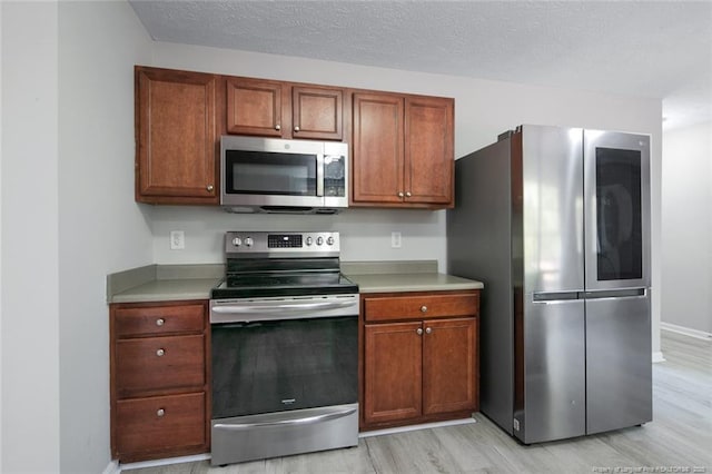 kitchen with stainless steel appliances, a textured ceiling, and light wood-type flooring