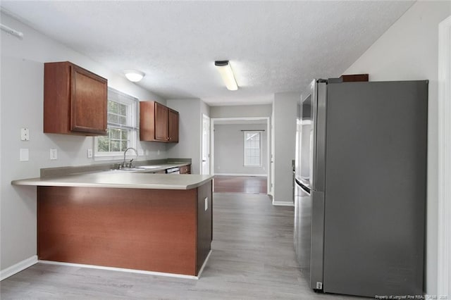 kitchen featuring sink, light hardwood / wood-style floors, stainless steel refrigerator, and kitchen peninsula