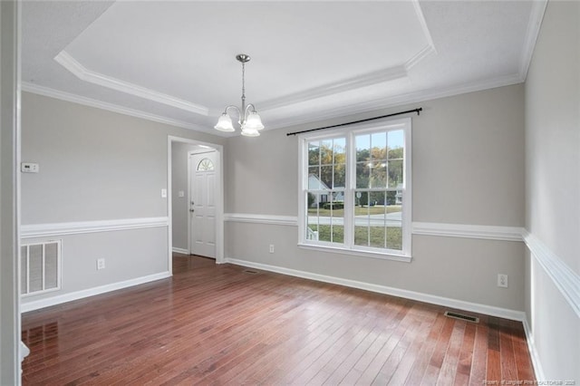 empty room featuring a raised ceiling, ornamental molding, dark hardwood / wood-style floors, and a chandelier