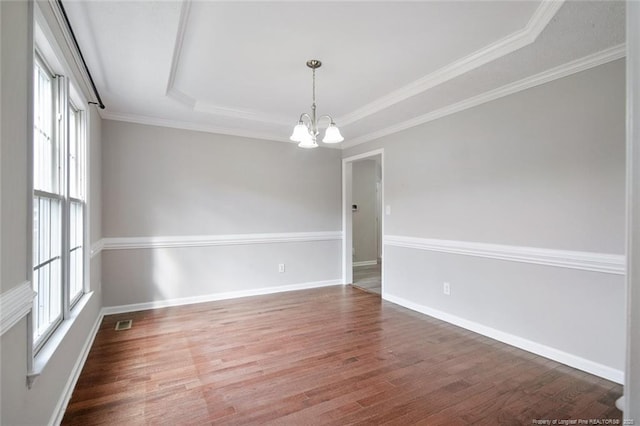 empty room featuring an inviting chandelier, ornamental molding, a tray ceiling, and dark wood-type flooring