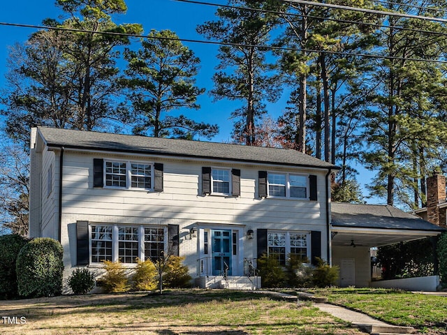 colonial-style house with brick siding, a carport, roof with shingles, and a front yard