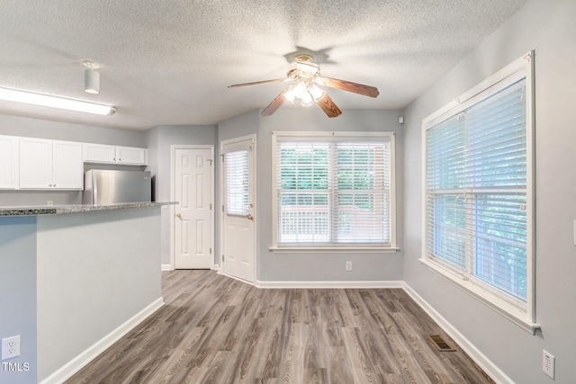 unfurnished dining area featuring ceiling fan, a textured ceiling, and light wood-type flooring