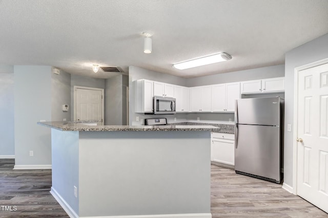 kitchen featuring dark stone countertops, stainless steel appliances, light hardwood / wood-style flooring, and white cabinets