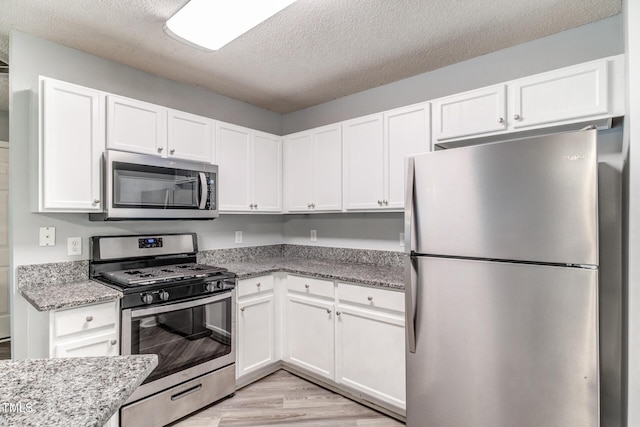 kitchen with stainless steel appliances, light stone counters, a textured ceiling, white cabinets, and light wood-type flooring