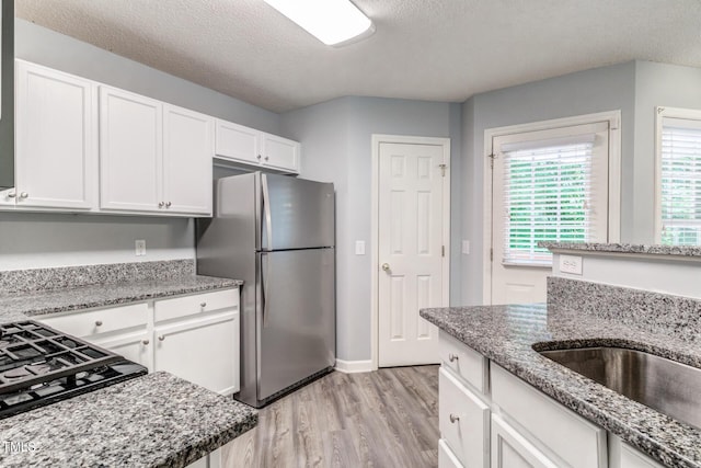 kitchen featuring light stone countertops, stainless steel fridge, light hardwood / wood-style floors, and white cabinets