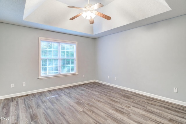 unfurnished room featuring ceiling fan, a tray ceiling, and light wood-type flooring