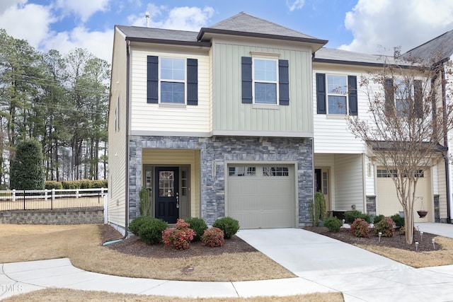 view of property featuring stone siding, fence, an attached garage, and concrete driveway