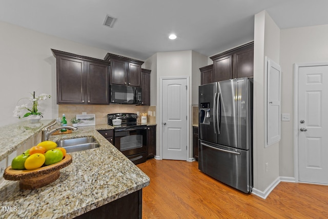 kitchen with sink, dark brown cabinets, light stone counters, black appliances, and light wood-type flooring