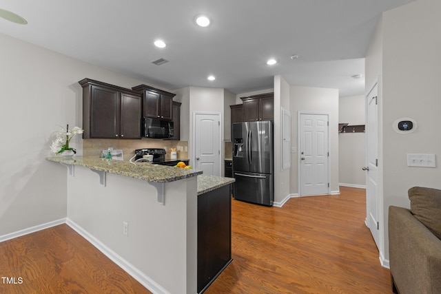 kitchen with hardwood / wood-style floors, black appliances, kitchen peninsula, and a kitchen bar