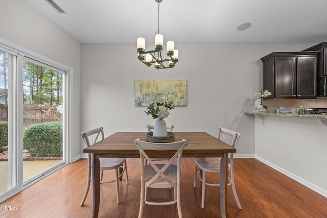 dining area with wood-type flooring, a healthy amount of sunlight, and an inviting chandelier