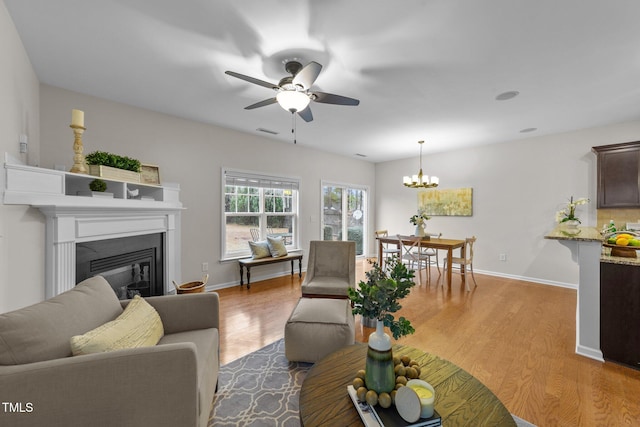 living room with ceiling fan with notable chandelier and light wood-type flooring