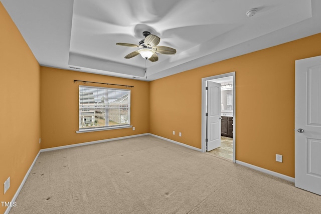 unfurnished bedroom with ceiling fan, connected bathroom, a tray ceiling, and light carpet