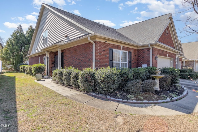 view of side of property featuring brick siding, a lawn, roof with shingles, and a garage