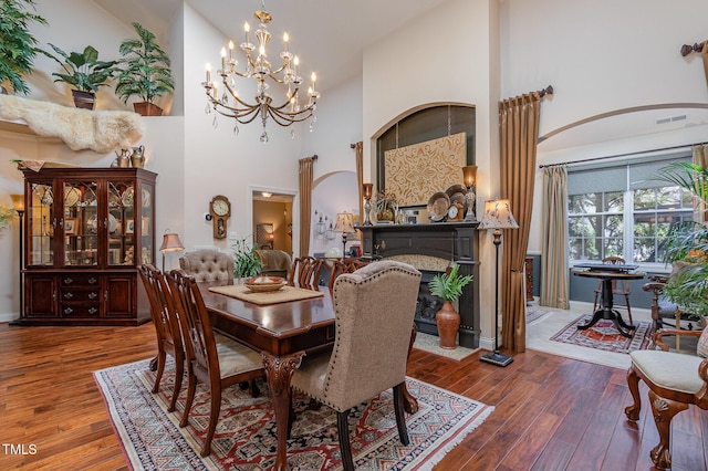 dining space featuring wood finished floors, baseboards, arched walkways, a premium fireplace, and a towering ceiling