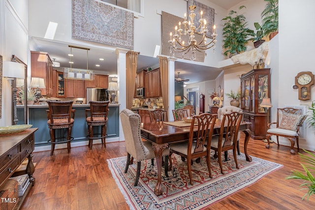 dining room with ornate columns, an inviting chandelier, a high ceiling, and dark wood-style flooring