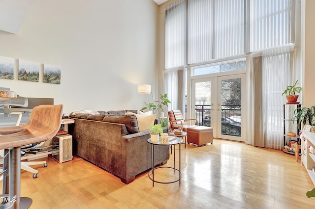 living room with french doors, a towering ceiling, and light hardwood / wood-style flooring