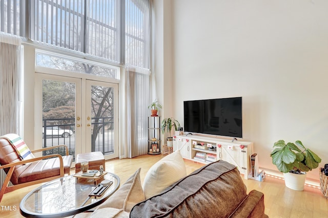 living room featuring a towering ceiling, light hardwood / wood-style floors, and french doors