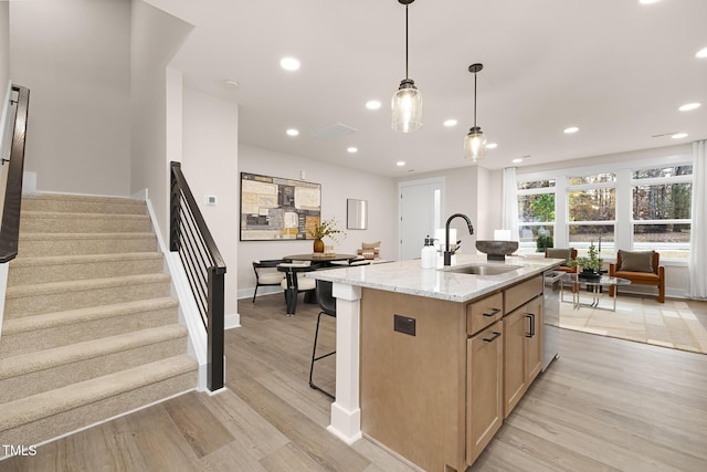 kitchen with sink, light stone countertops, light hardwood / wood-style floors, and a center island with sink