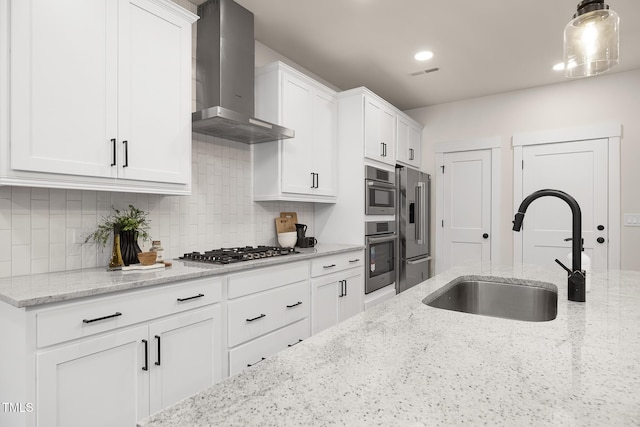 kitchen with sink, stainless steel appliances, light stone countertops, white cabinets, and wall chimney exhaust hood