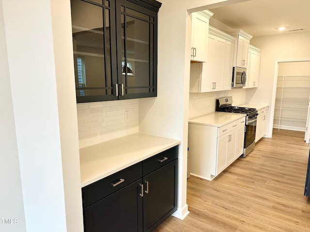 kitchen with dark cabinets, stainless steel appliances, light countertops, light wood-style floors, and white cabinetry