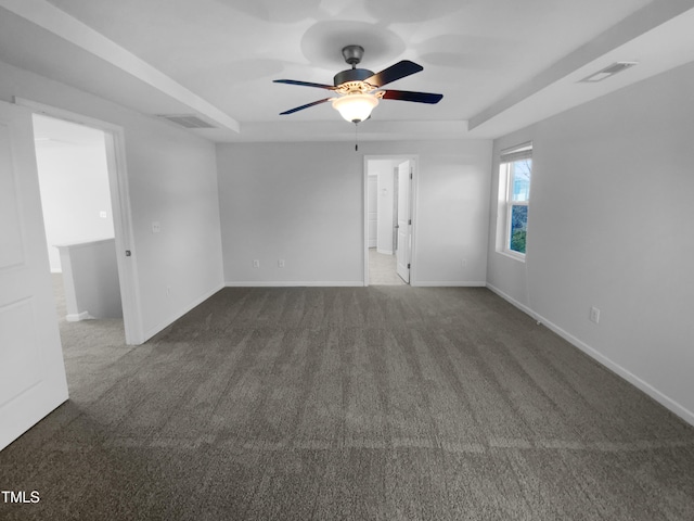 empty room with a tray ceiling, ceiling fan, and dark colored carpet