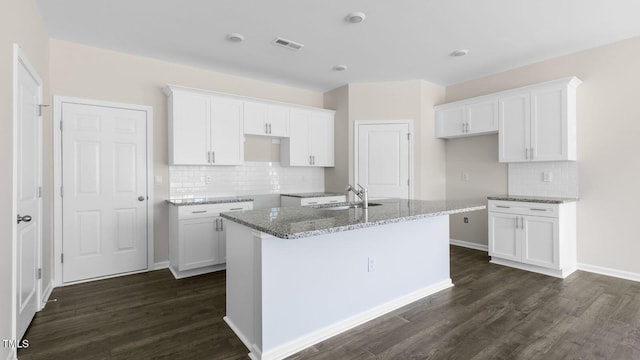 kitchen with sink, white cabinetry, a kitchen island with sink, dark hardwood / wood-style floors, and light stone countertops