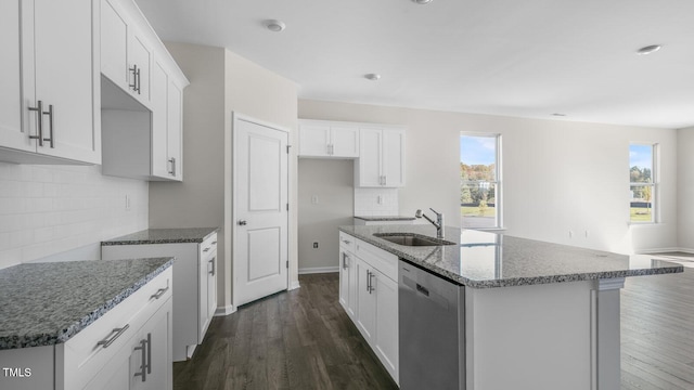 kitchen with white cabinetry, dishwasher, sink, dark stone counters, and a center island with sink