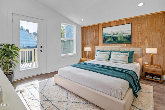 bedroom featuring wooden walls, vaulted ceiling, hardwood / wood-style floors, and access to outside