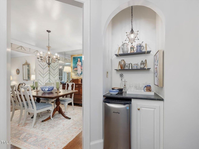 bar featuring ornamental molding, refrigerator, a chandelier, and decorative light fixtures