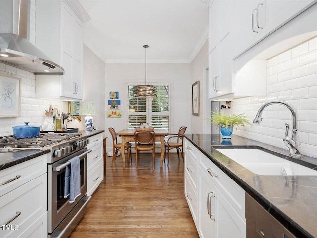 kitchen featuring pendant lighting, sink, white cabinets, gas range, and wall chimney exhaust hood