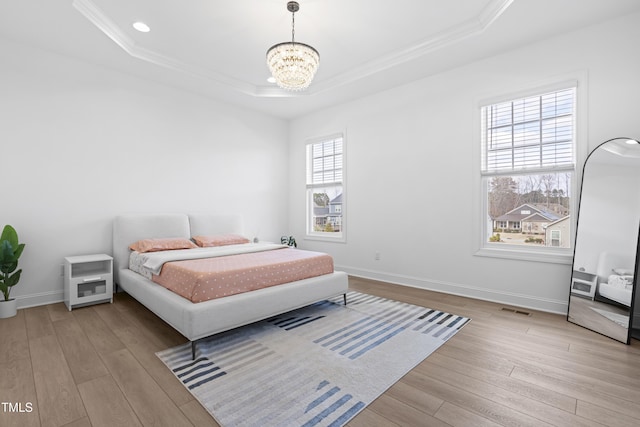 bedroom with a tray ceiling, visible vents, crown molding, and wood finished floors