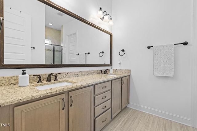 full bathroom featuring double vanity, a stall shower, baseboards, and a sink