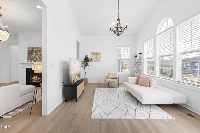 living area with an inviting chandelier, plenty of natural light, light wood finished floors, and a glass covered fireplace