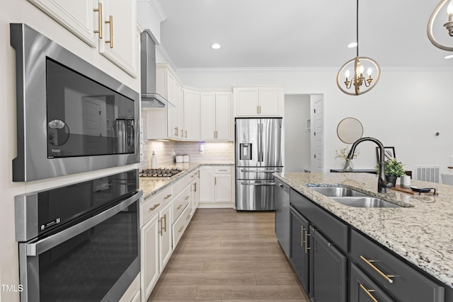 kitchen with appliances with stainless steel finishes, white cabinets, a sink, and wall chimney exhaust hood