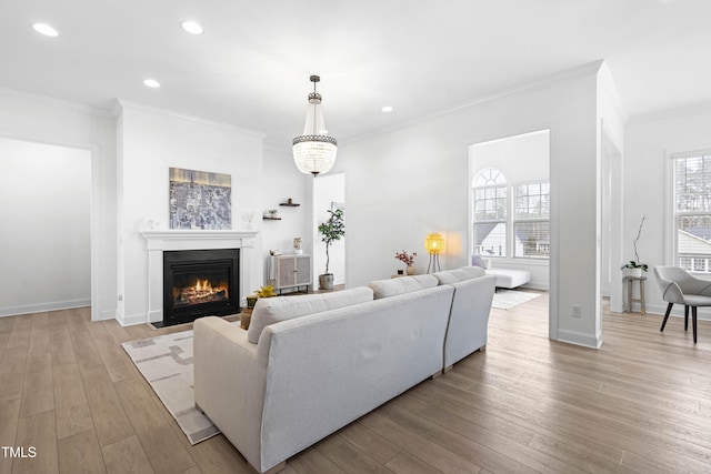 living room featuring light wood-type flooring, a fireplace with flush hearth, crown molding, and recessed lighting