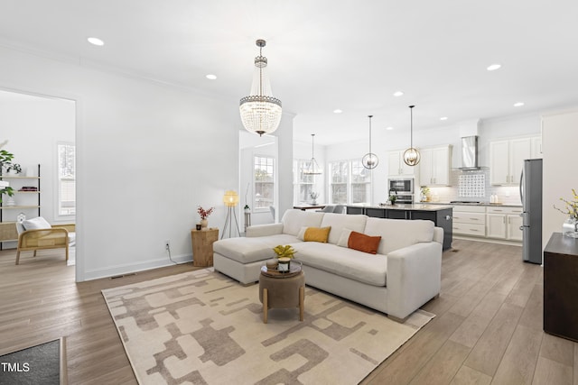 living room with light wood finished floors, visible vents, baseboards, crown molding, and recessed lighting