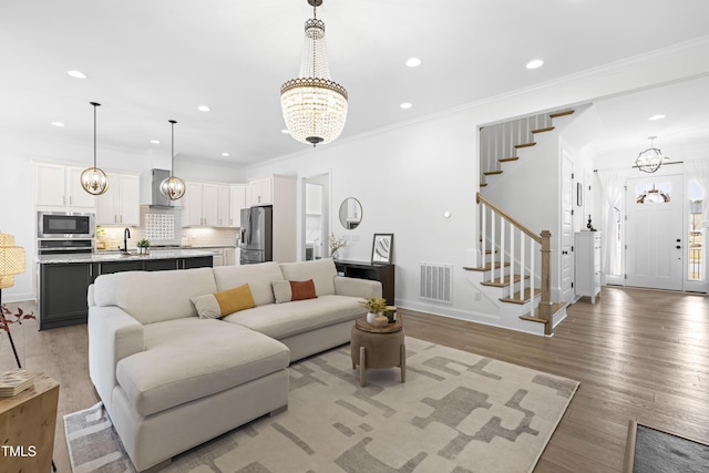 living area with a notable chandelier, visible vents, light wood-style flooring, ornamental molding, and stairs