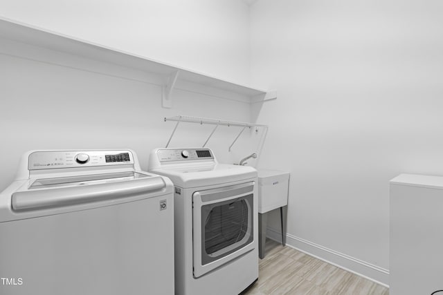 clothes washing area featuring laundry area, light wood finished floors, washing machine and clothes dryer, and baseboards