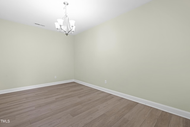 spare room with an inviting chandelier, baseboards, visible vents, and wood finished floors