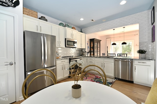 kitchen with decorative light fixtures, dark stone countertops, stainless steel appliances, light hardwood / wood-style floors, and white cabinets