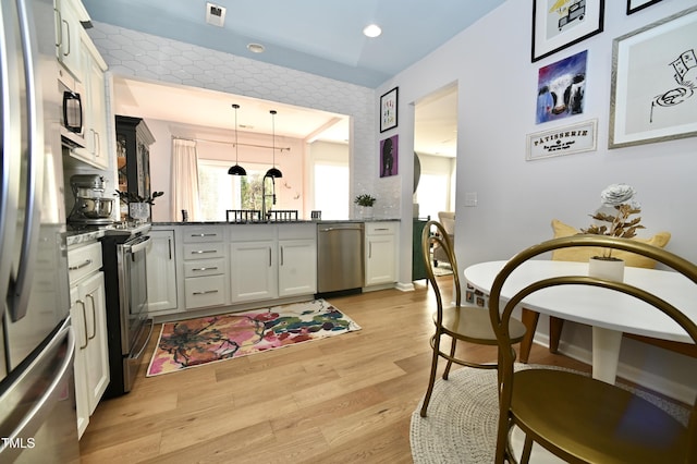 kitchen with sink, white cabinetry, decorative light fixtures, light hardwood / wood-style flooring, and appliances with stainless steel finishes